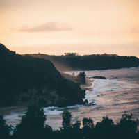 a high view of a tropical beach at dusk, silhouettes of trees and cliffs